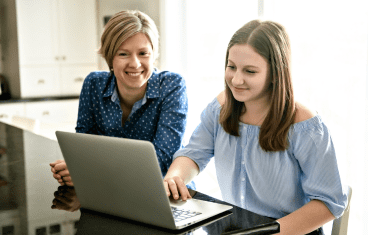 Two women engaged in conversation while sitting at a table, with a laptop open between them.