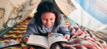 A young girl engrossed in a book while sitting inside a cozy tent, surrounded by soft lighting and a peaceful atmosphere.