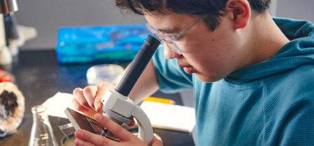 A young man intently examines a specimen through a microscope in a laboratory setting.