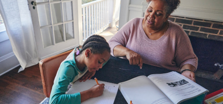 A woman and a child are seated at a table, engaged in reading a book together, fostering a moment of learning and connection.