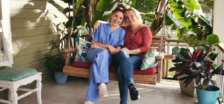 Two women relax on a porch swing, enjoying each other's company in front of a charming house.