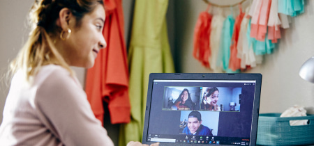 A woman engaged in a video chat with friends, using her laptop in a cozy indoor setting.