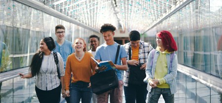 A diverse group of young individuals walking together down a brightly lit hallway, engaged in conversation and laughter.