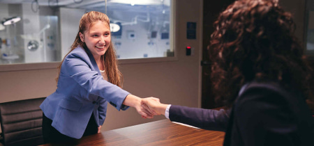 A woman and another woman shake hands in a professional office setting, symbolizing collaboration and agreement.