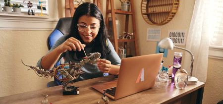 A woman seated at a desk, focused on her laptop, with a colorful toy placed beside her, creating a lively workspace.