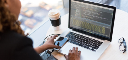 A person focused on a laptop screen displaying lines of code, engaged in programming or software development.