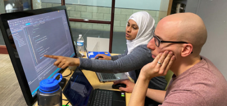 Two individuals collaborating on a computer, focused on the monitor in front of them, engaged in productive work.