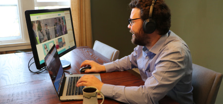 A man with headphones sits at a table, focused on his laptop, immersed in his work or entertainment.