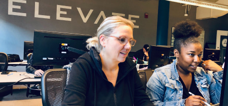 Two women collaborating at a computer in a modern office setting, engaged in a productive discussion.