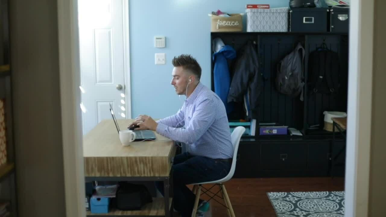 A man seated at a desk in a well-lit room, focused on his work with papers and a laptop in front of him.