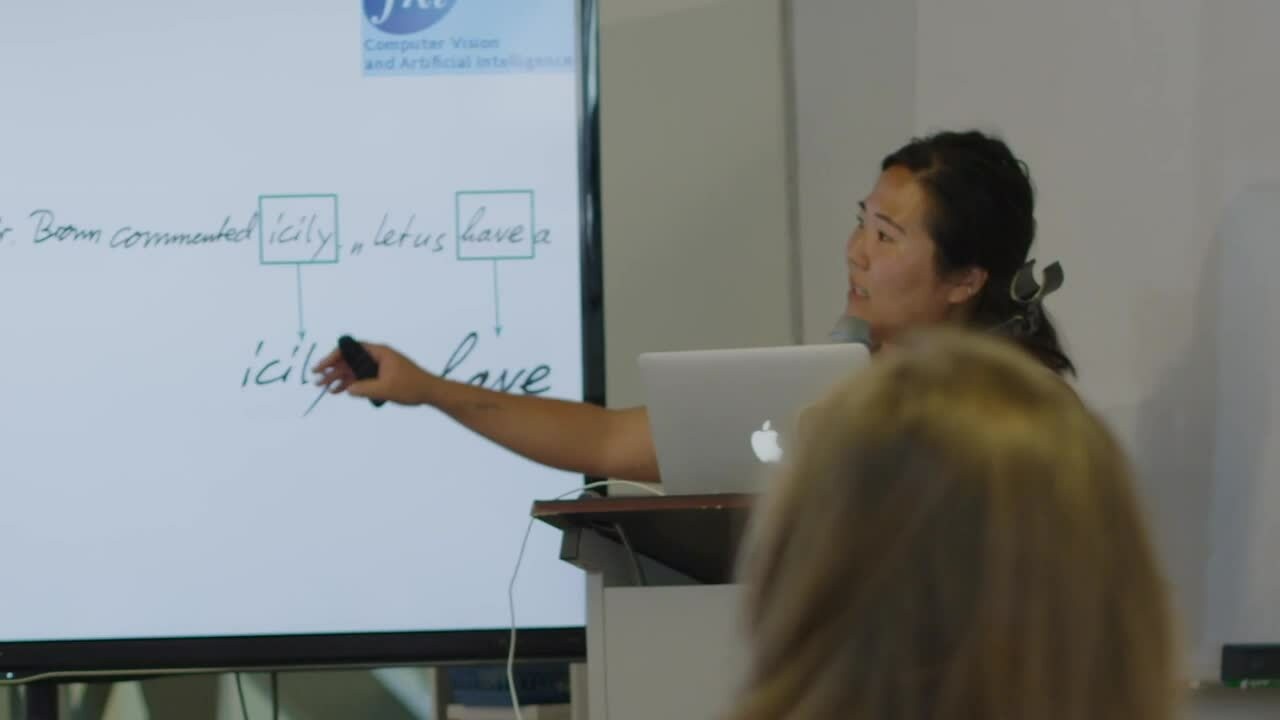  A woman stands confidently, presenting in front of a whiteboard filled with notes and diagrams, engaging her audience.