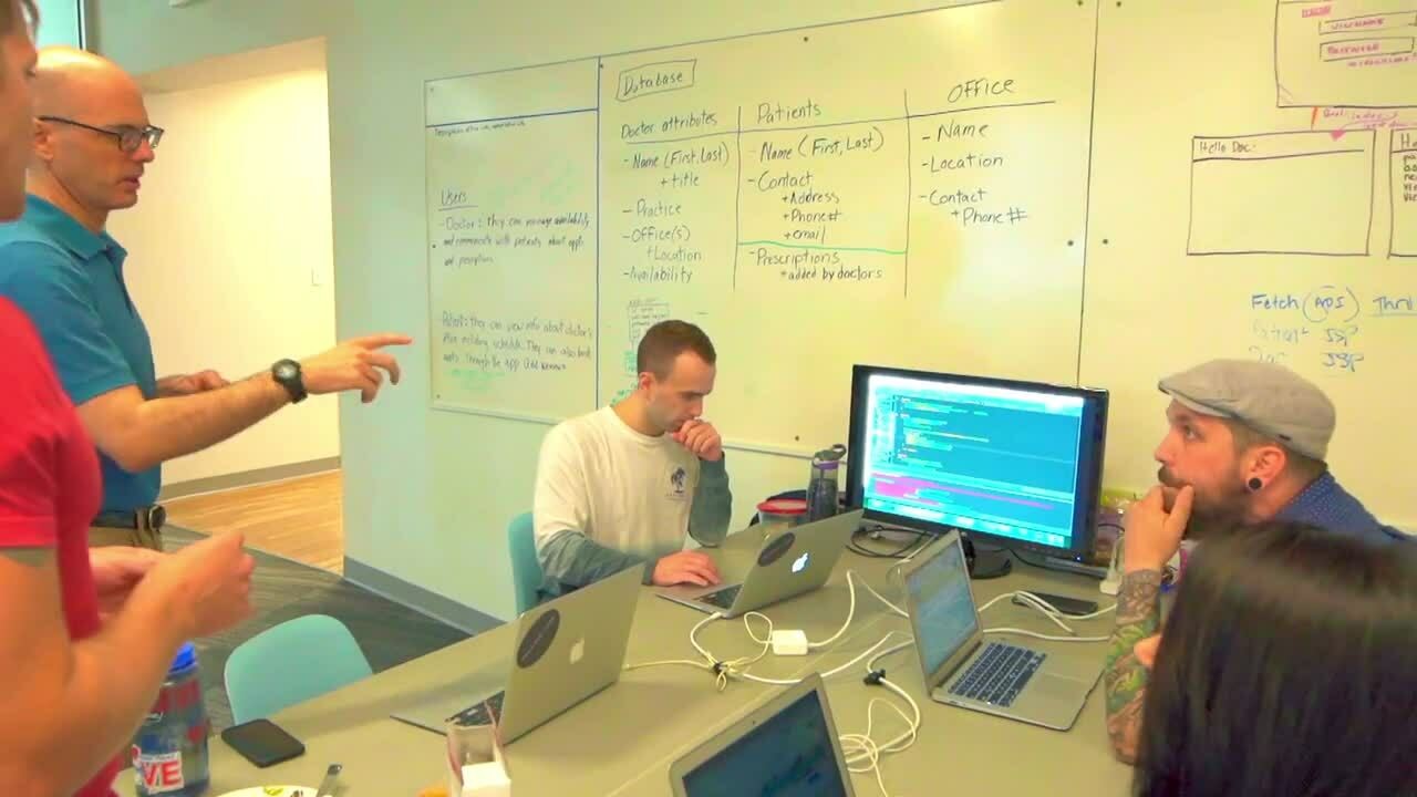 A diverse group of individuals engaged in discussion while using laptops at a round table in a collaborative setting.